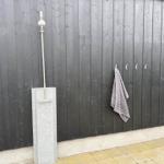 Außen-Dusche mit Duschbrause und Wandhalterung an dunklem Holzzaun.