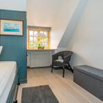Schlafzimmer mit Bett, Stuhl und Fenster. Holzboden und Wand mit Bild.