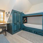 Schlafzimmer mit Doppelstockbett, Schrank und Fenster mit Sitzbank.