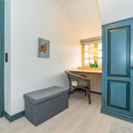 Ein Raum mit blauer Tür, grauem Sitzkasten und Schreibtisch unter dem Fenster.
