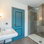 Badezimmer mit Dusche, Waschbecken und blauer Tür.