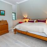 Schlafzimmer mit Holzbett, Nachttischen und Schrank. Wandbilder und Fenster sichtbar.