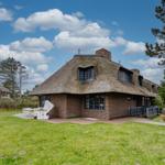 Haus mit Strohdach, Garten und Terrasse unter blauem Himmel.