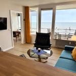 Wohnzimmer mit Blick aufs Meer und Balkon. Sofa, Sessel und Fernseher.