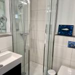 Badezimmer mit Dusche, Waschbecken und Toilette. Weiße Fliesen und Glaswand.