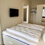 Schlafzimmer mit Doppelbett, Wand-TV und Kleiderschrank mit Spiegel.