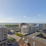 Panoramablick auf Strand, Meer und Stadt mit mehreren Gebäuden und Parkplätzen.