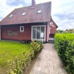 Rotes Haus mit Garten, Terrasse und Dachfenstern. Pfad führt zur Eingangstür.