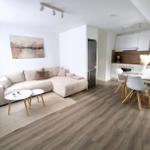 Wohn- und Essbereich mit Sofa, Esstisch und Küchenzeile. Holzdielenboden und weiße Wände.