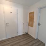 Flur mit Tür zu privatem Raum und WC, Holzpaneel an Wand, Heizkörper und Holzdielenboden.