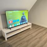 Fernseher auf weißem TV-Board in einem Raum mit Holzdielen und schräger Decke.