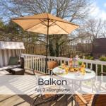 Terrasse mit Sonnenschirm, Esstisch und Liege. Blick auf Wald und Haus.
