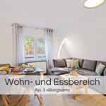 Wohn- und Essbereich mit Sofa, Tisch und TV. Fenster mit Blick auf Wald.
