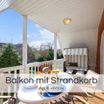 Balkon mit Tisch, Stühlen und Strandkorb. Blick auf Grünflächen und Häuser.