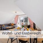 Wohn- und Essbereich mit Sofa, Tisch und Stühlen. Fenster mit rosa Vorhängen.