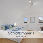 Schlafzimmer mit Doppelbett, zwei Fenstern und Sitzgelegenheit.