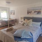 Schlafzimmer mit Bett, Schreibtisch und Fenster. Wandbilder zeigen Strand.