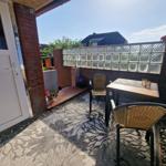 Terrasse mit Tisch, zwei Stühlen, Teppich und Glasblockwand.
