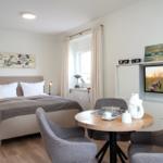 Schlafzimmer mit Bett, Esstisch und Fernseher. Fenster mit Vorhängen. Wandbilder und Möbel.