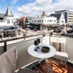 Terrasse mit Tisch und Stühlen, Blick auf belebten Platz mit Geschäften und Passanten.