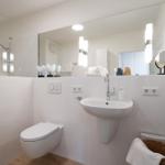 Badezimmer mit Toilette, Waschbecken und Dusche. Weiße Fliesen und Spiegel.