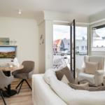 Wohnzimmer mit Sofa, Sitzgruppe und TV. Terrasse mit Blick auf Gebäude.