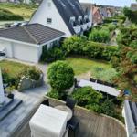 Terrasse mit Tisch und Stühlen, umgeben von Grünflächen und einem Gartenhaus.