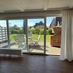 Räumlichkeiten mit Holzboden und Glasfront zum Garten mit Sitzmöbeln.