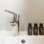 Waschbecken mit Wasserhahn und drei Flaschen mit Pflegeprodukten.