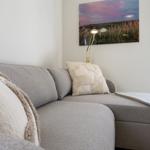 Graße Couch mit Kissen und Decke. Wandbild und Fenster mit Blick.
