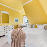 Schlafzimmer mit gelben Wänden, weißem Bett und Schrank. Fenster mit Blick nach draußen.