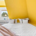Schlafzimmer mit gelben Wänden, weißem Bett und Fenster mit Blick auf Bäume.