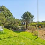 Grüner Garten mit weißem Holzstuhl, Bäumen und Blick auf Ferienhaus im Hintergrund.