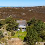 Haus mit Strohdach unter Bäumen, Blick auf Dünen und Meer.