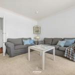 Wohnzimmer mit grauem Sofa, weißen Möbeln und Wandbild.