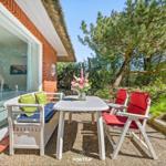 Terrasse mit weißem Tisch, zwei roten Stühlen und einer Bank mit grünen Kissen.
