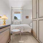 Schlafzimmer mit Bett, Schrank und Fenster mit Blick auf Bäume.