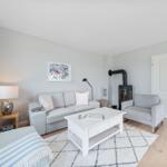 Wohnzimmer mit Sofa, Sessel, Kaminofen und Holzboden.
