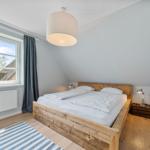 Schlafzimmer mit Holzbett, Fenster und Deckenlampe.