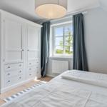Schlafzimmer mit weißem Schrank, Bett und Fenster mit Blick auf Grün.