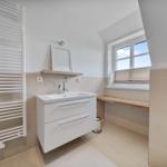 Badezimmer mit Waschbecken, Spiegel, Fenster und Heizkörper.