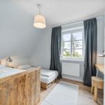 Schlafzimmer mit Holzbett, Fenster, Vorhängen und Schreibtisch.