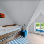 Ein Schlafzimmer mit Holzbett, blauem Nachttisch und Fenster mit Blick auf Grün.