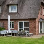 Haus mit Strohdach, Terrasse mit Sitzgruppe und Tisch, Grasfläche und Bäume im Hintergrund.