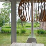 Durch große Fenster blickt man auf einen grünen Garten mit Bäumen und eine Backsteinmauer.
