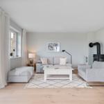 Wohnzimmer mit Sofa, Sessel und Kaminofen. Holzboden und helle Wände.