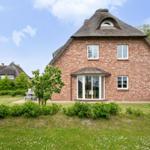 Rotes Backsteinhaus mit Strohdach und Fensterfront im Garten.
