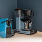 Eine blaue Nespresso-Kaffeemaschine und eine Moccamaster-Kaffeemaschine auf einer Arbeitsplatte.