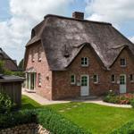 Ein Haus mit strohgedecktem Dach, roten Ziegeln und einem gepflegten Garten.