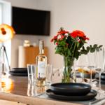 Esstisch mit schwarzen Tellern, Weingläsern und Blumenarrangement.